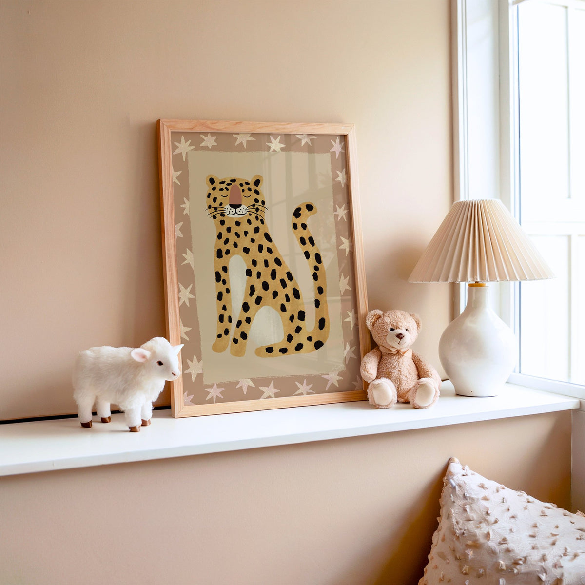 Smiling leopard with star border nursery print in an oak frame on a window ledge with a toy lamb and teddy