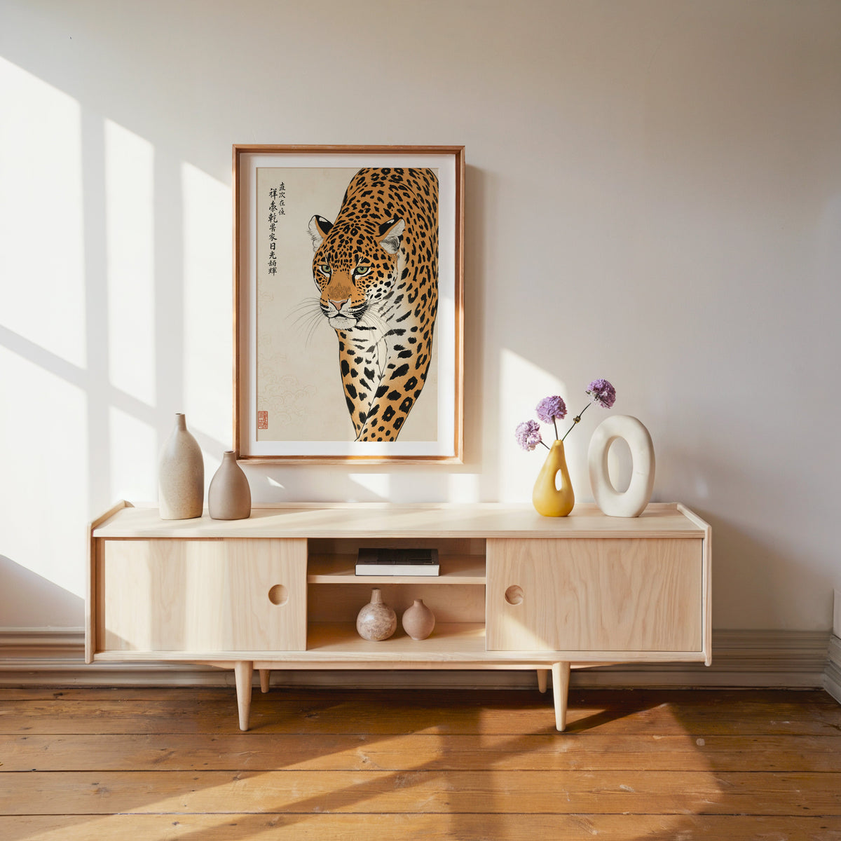 prowling leopard with calligraphy print shown in a wood frame with a white mat above a pale wood media console