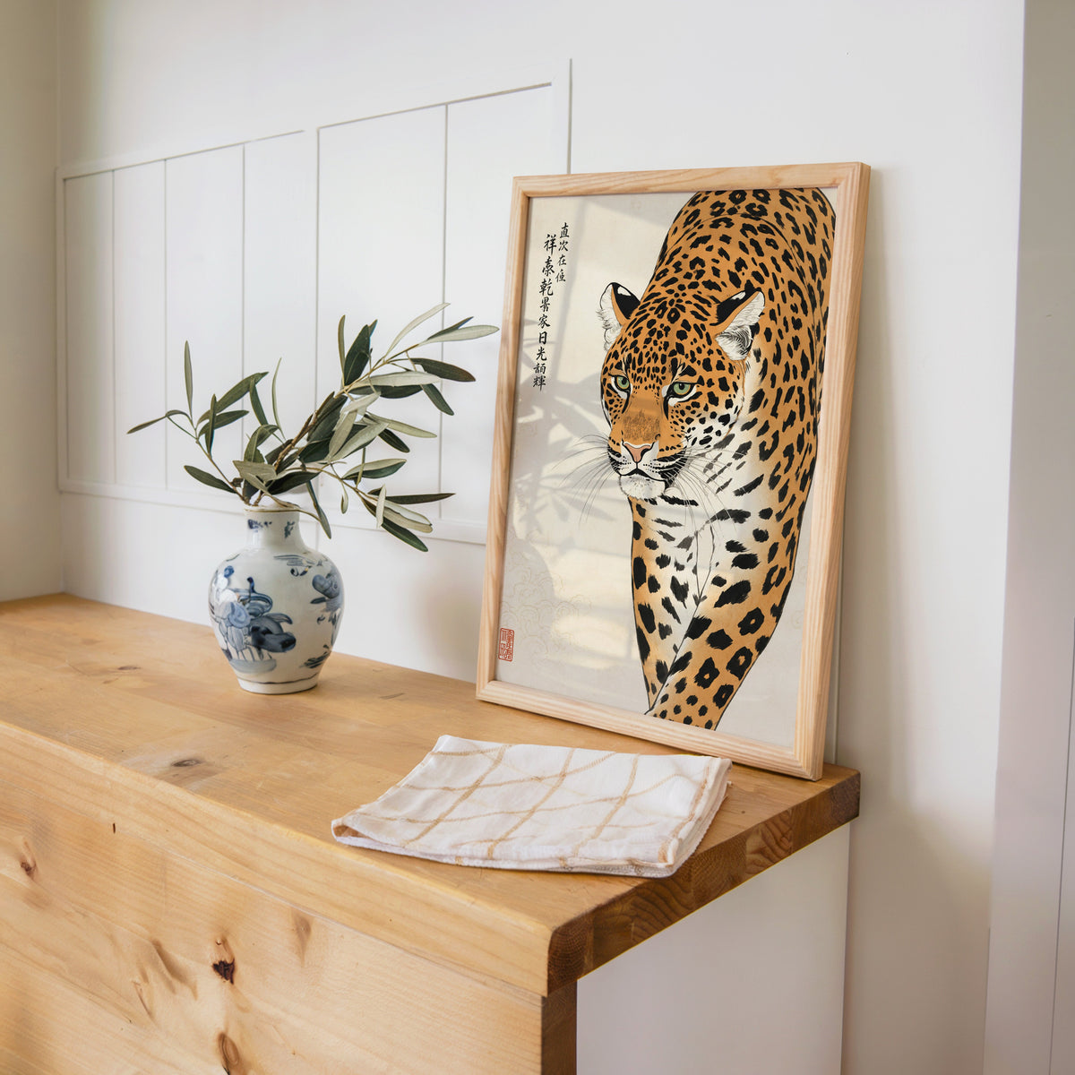 prowling leopard with calligraphy print in a pine frame on a wooden counter beside a blue and white porcelain vase