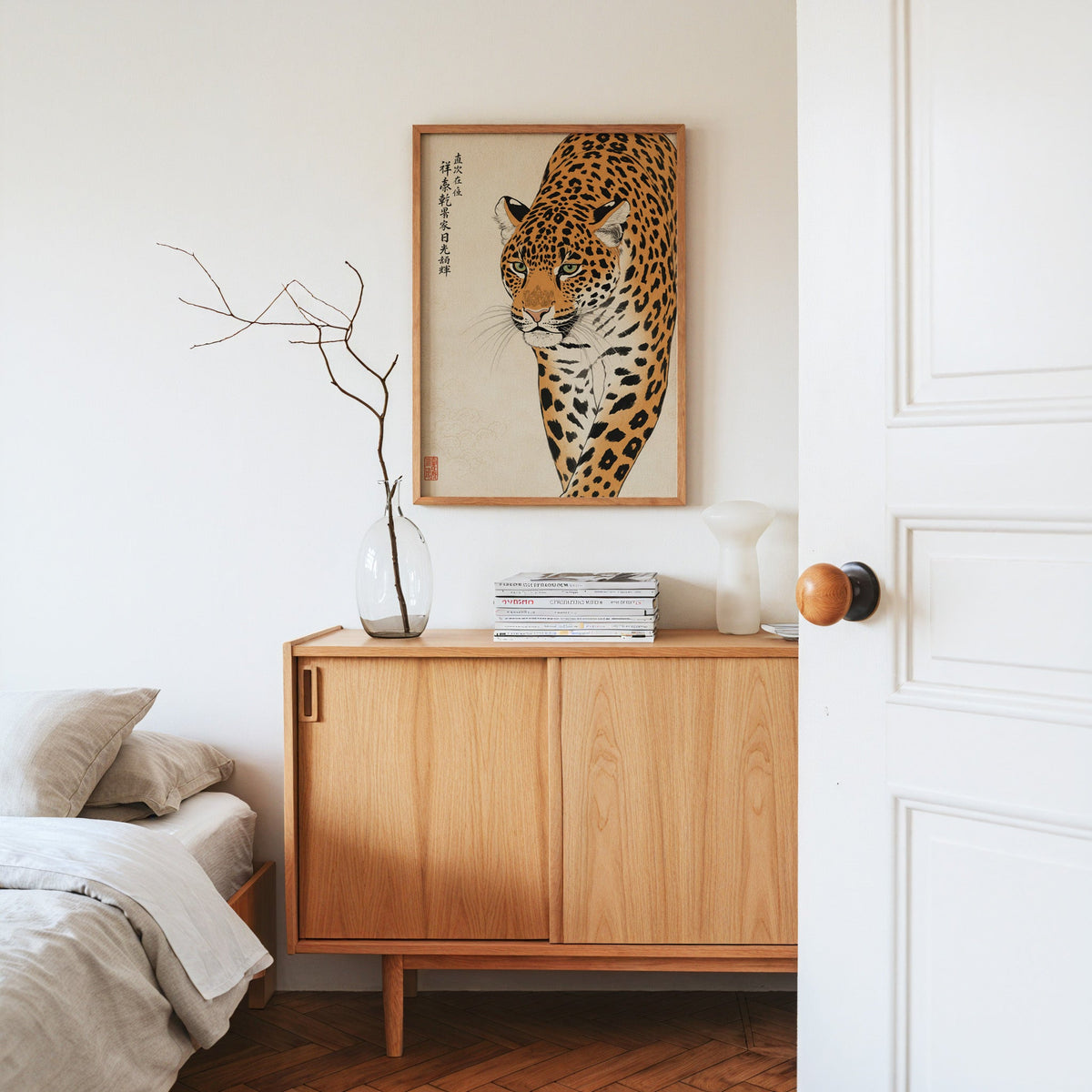 prowling leopard with calligraphy print in an oak frame above an oak sideboard in a bedroom with linen bedding
