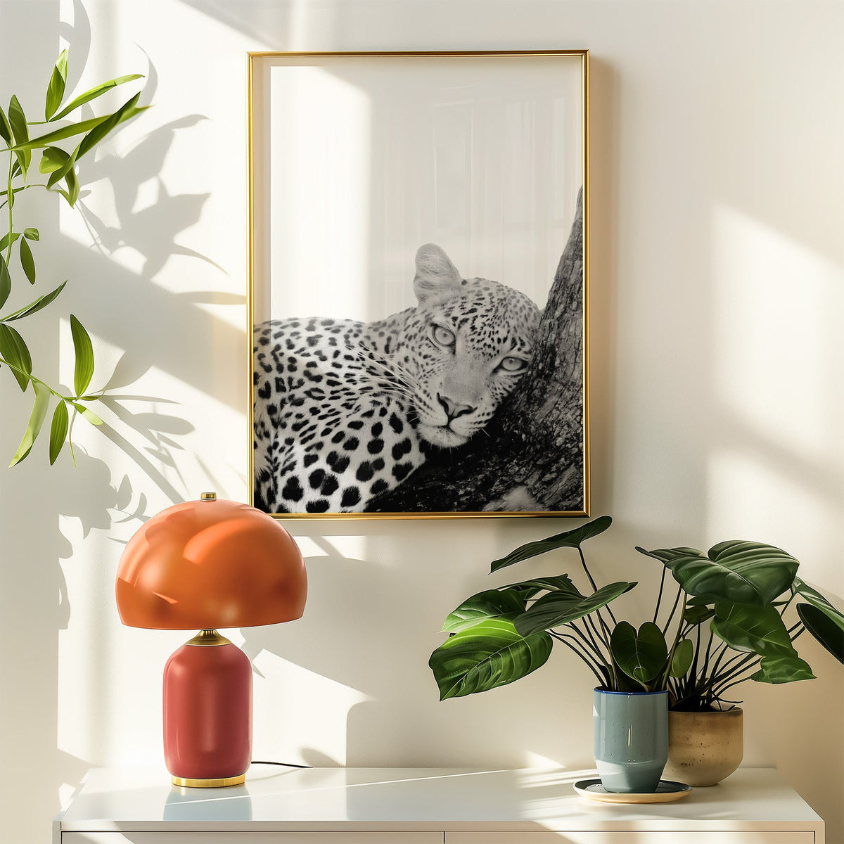 Leopard resting head on tree trunk black and white print shown in a gold frame above a white sideboard with an orange lamp