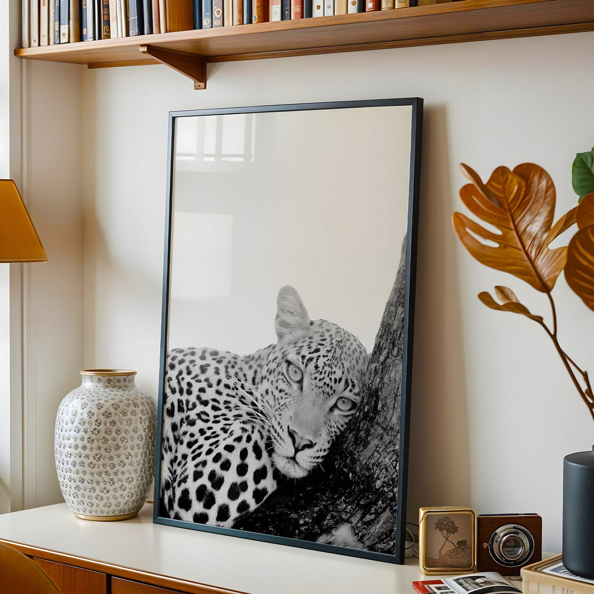 Leopard resting head on tree trunk black and white print in a black frame on a console under a bookshelf