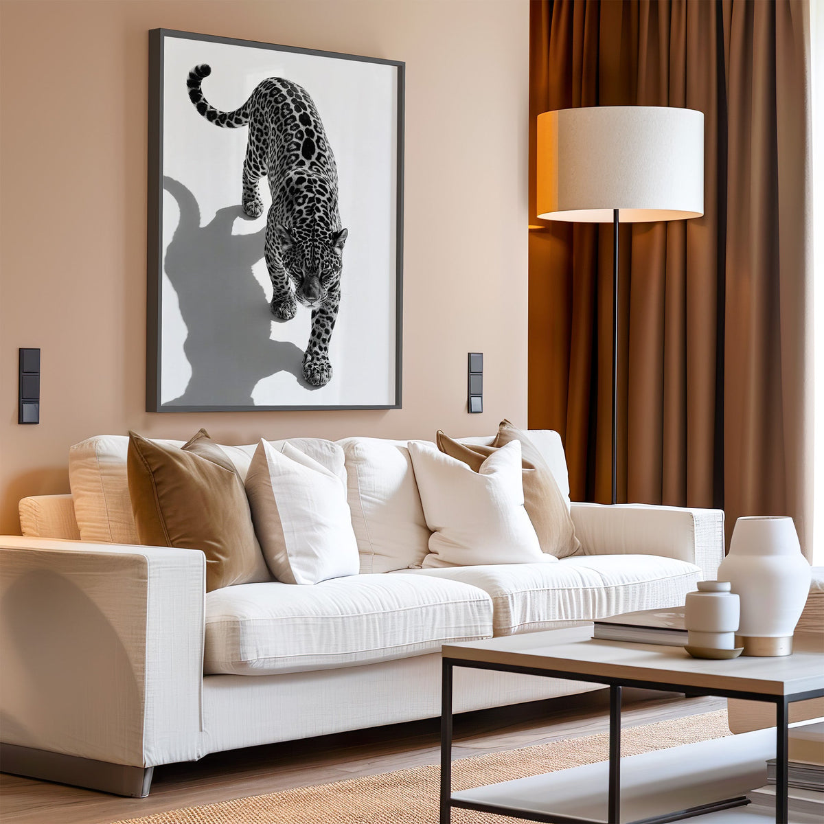 Stalking leopard from above with shadow print in a black frame above a cream sofa on a blush living room wall