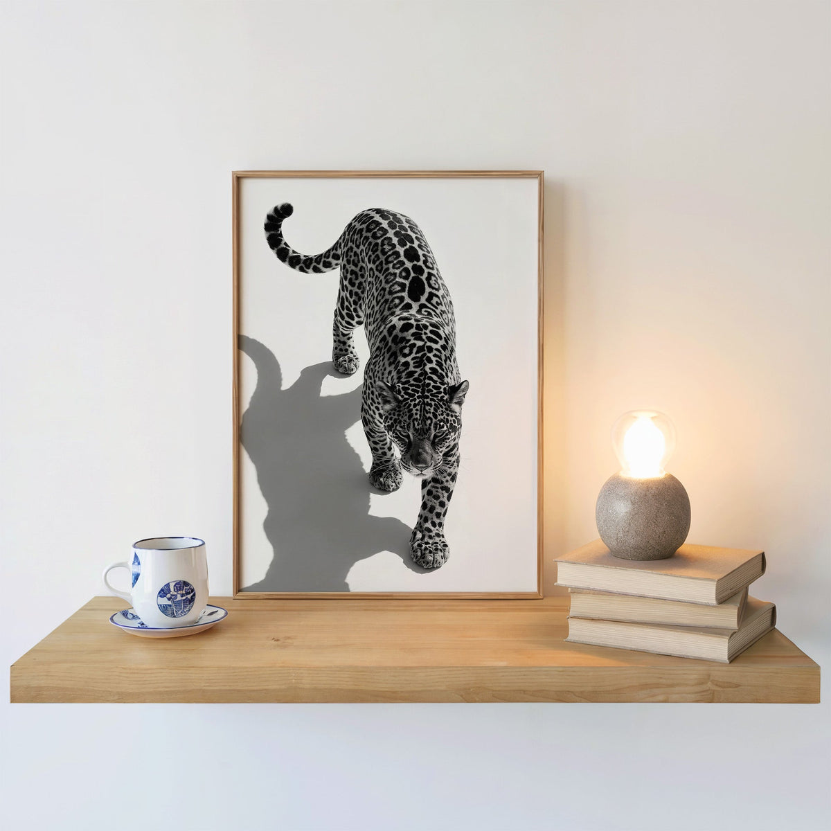 Stalking leopard from above with shadow print in an oak frame on a floating shelf beside a glowing lamp