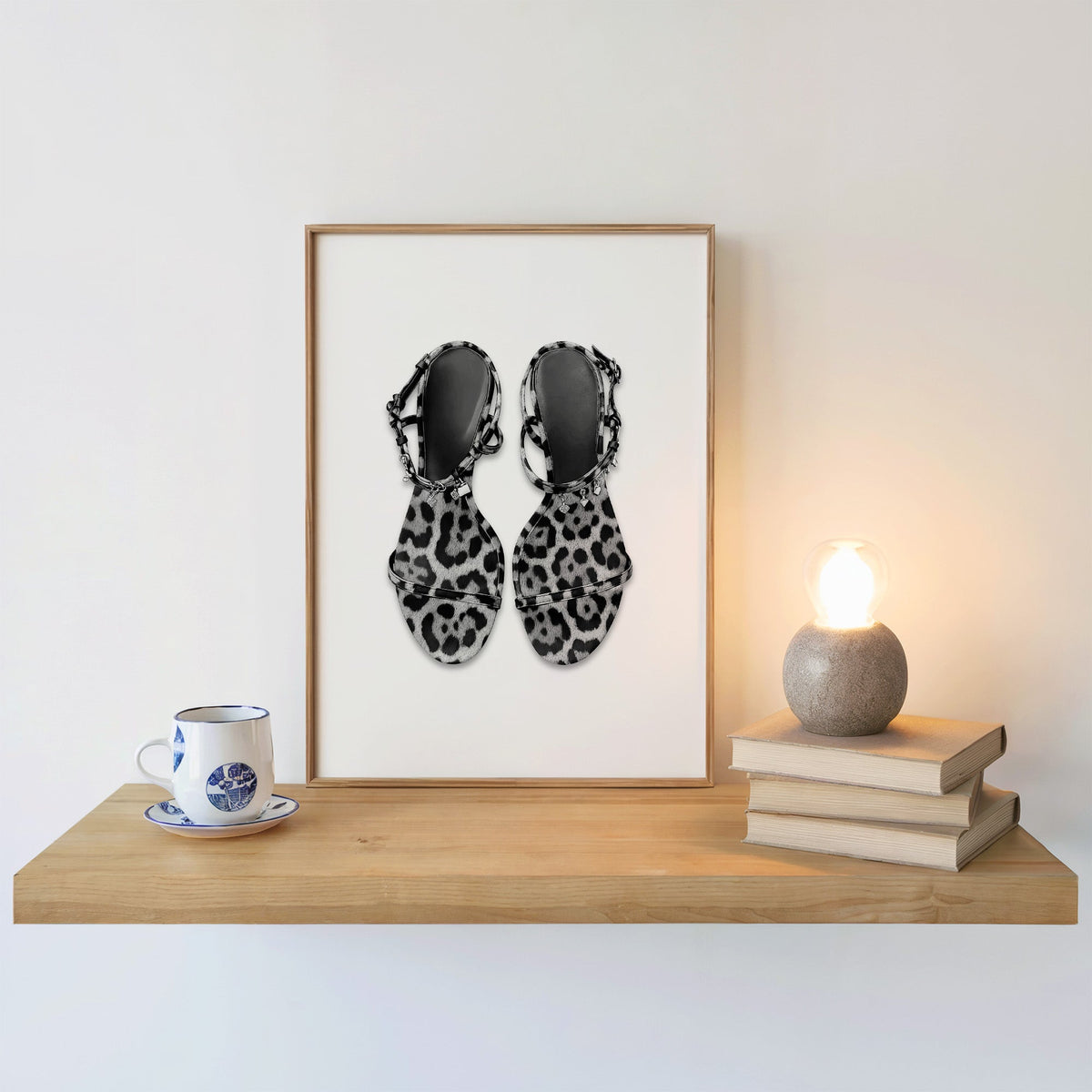 Top-down leopard strappy sandals with charms print in an oak frame on a floating shelf beside a glowing lamp