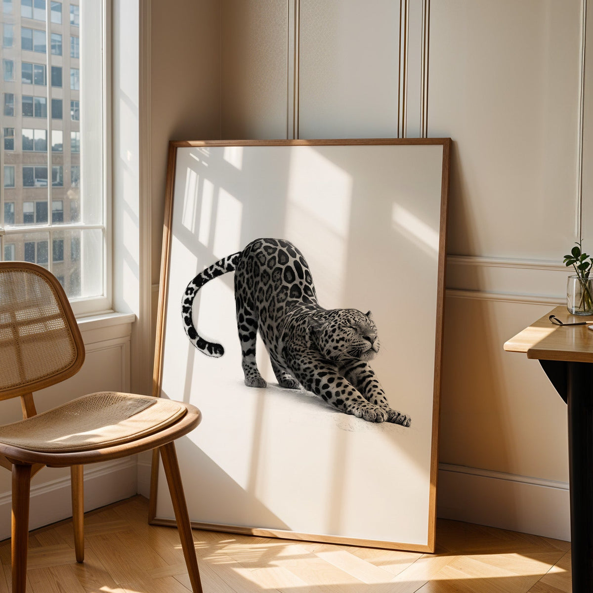 Stretching leopard with curled tail print in an oak frame leaning in a sunlit corner beside a cane chair
