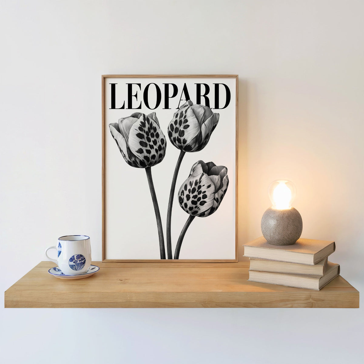 Three leopard-spotted tulips with LEOPARD title print in an oak frame on a floating shelf beside a glowing lamp