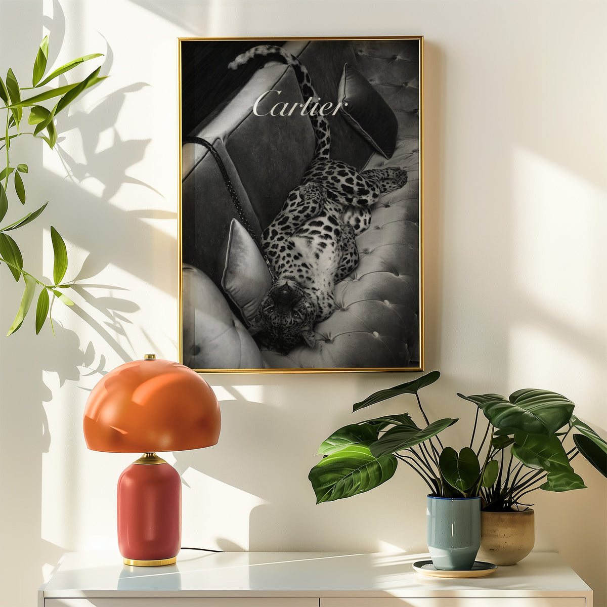 Leopard lounging on tufted velvet sofa print shown in a gold frame above a white sideboard with an orange lamp