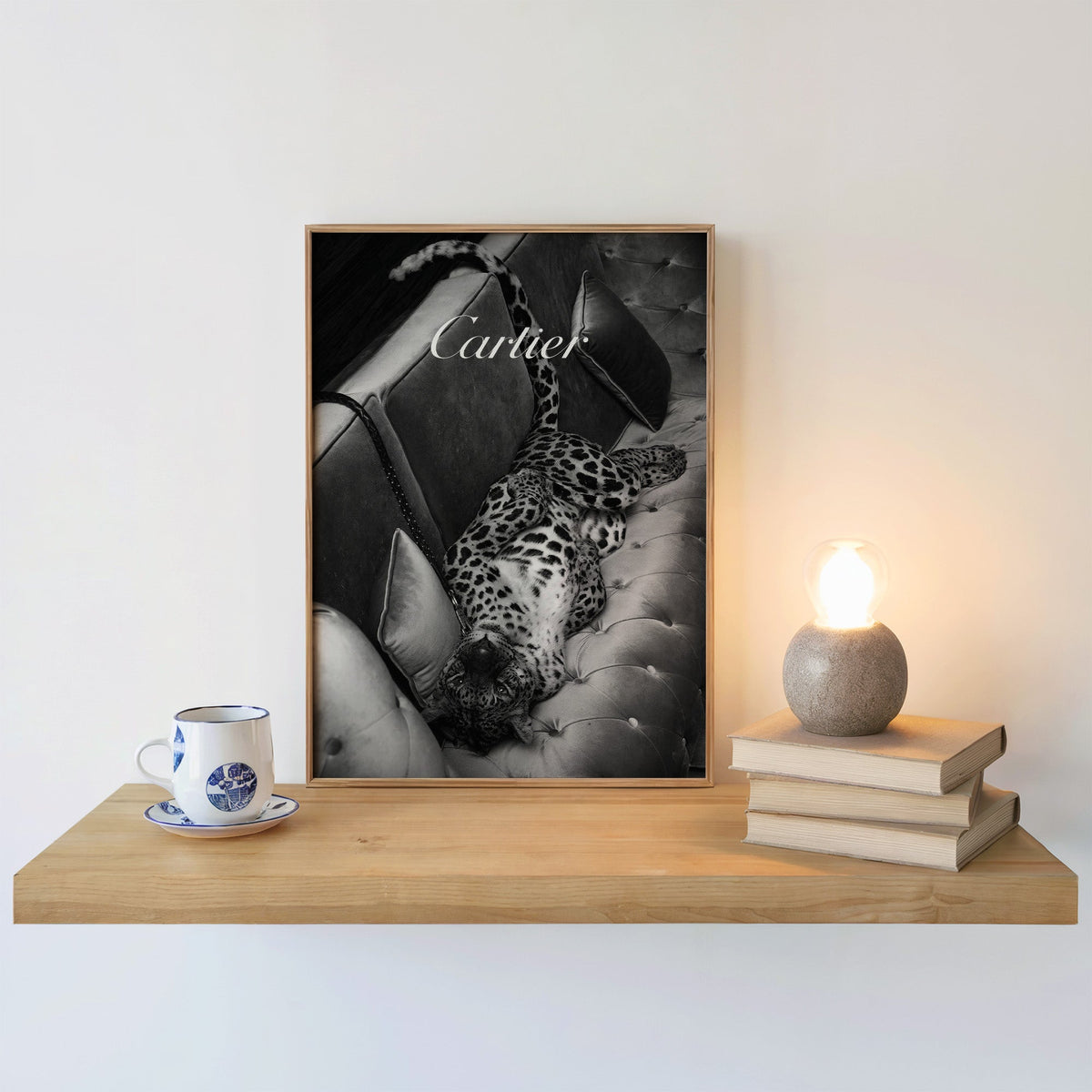 Leopard lounging on tufted velvet sofa print in an oak frame on a floating shelf beside a glowing lamp