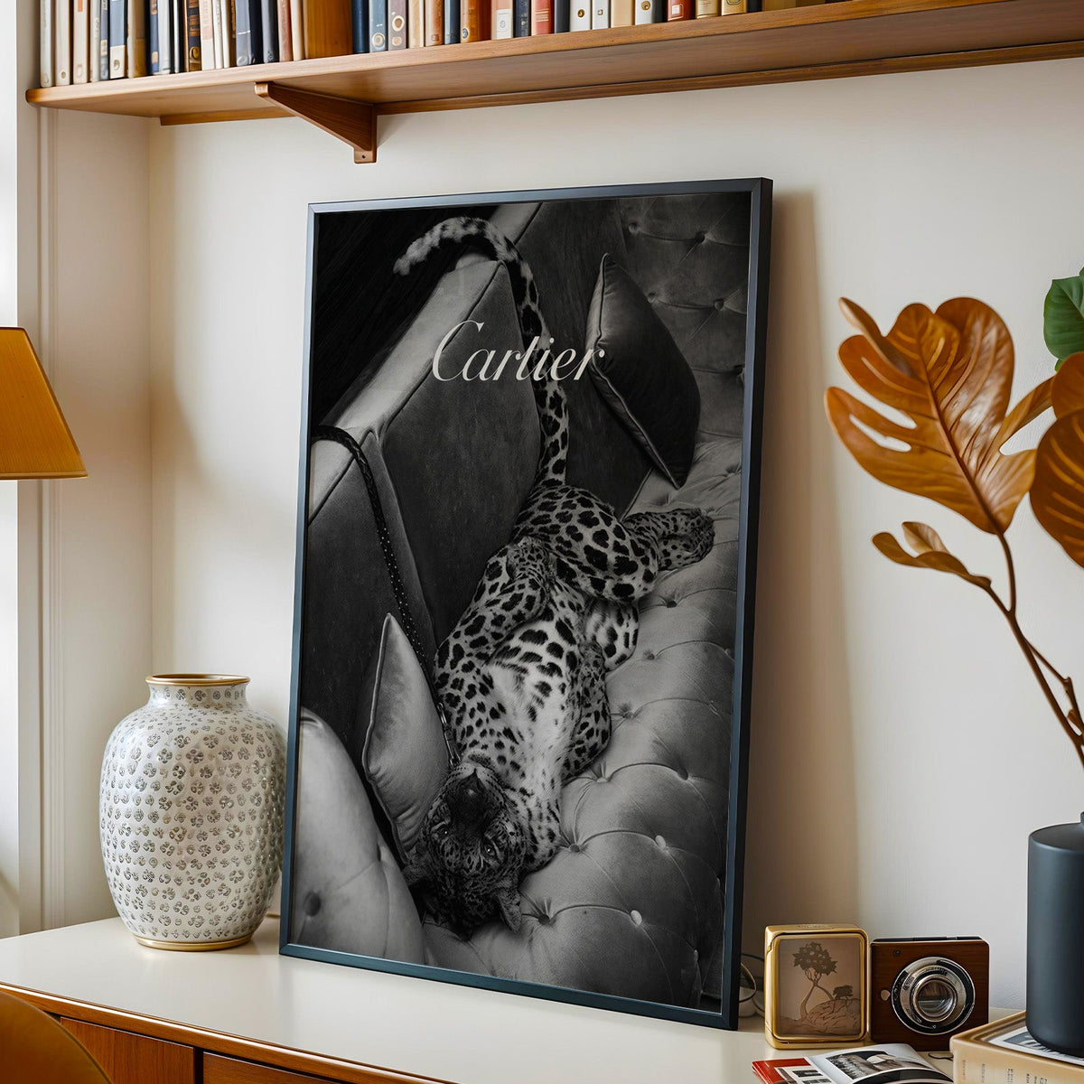 Leopard lounging on tufted velvet sofa print in a black frame on a console under a bookshelf