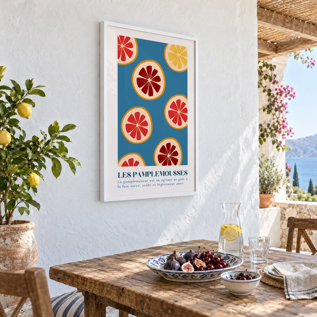 LES PAMPLEMOUSSES grapefruit slices petrol blue print in a white frame on a whitewashed terrace wall above a lunch table with figs and cherries, seen at an angle