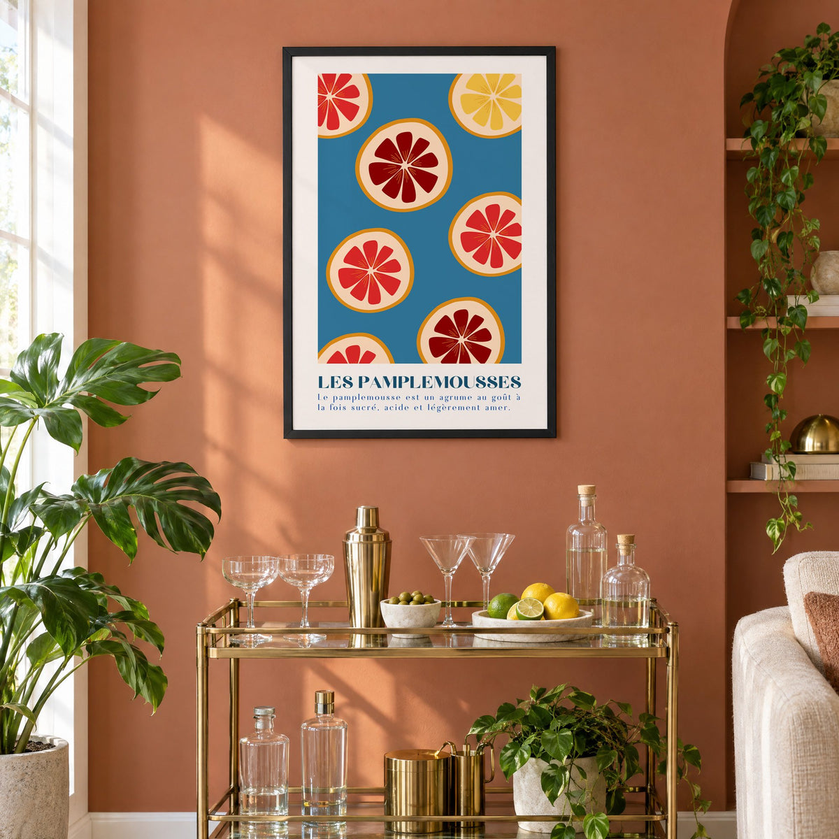 LES PAMPLEMOUSSES grapefruit slices petrol blue print in a black frame on a terracotta wall above a brass bar cart with coupes and citrus