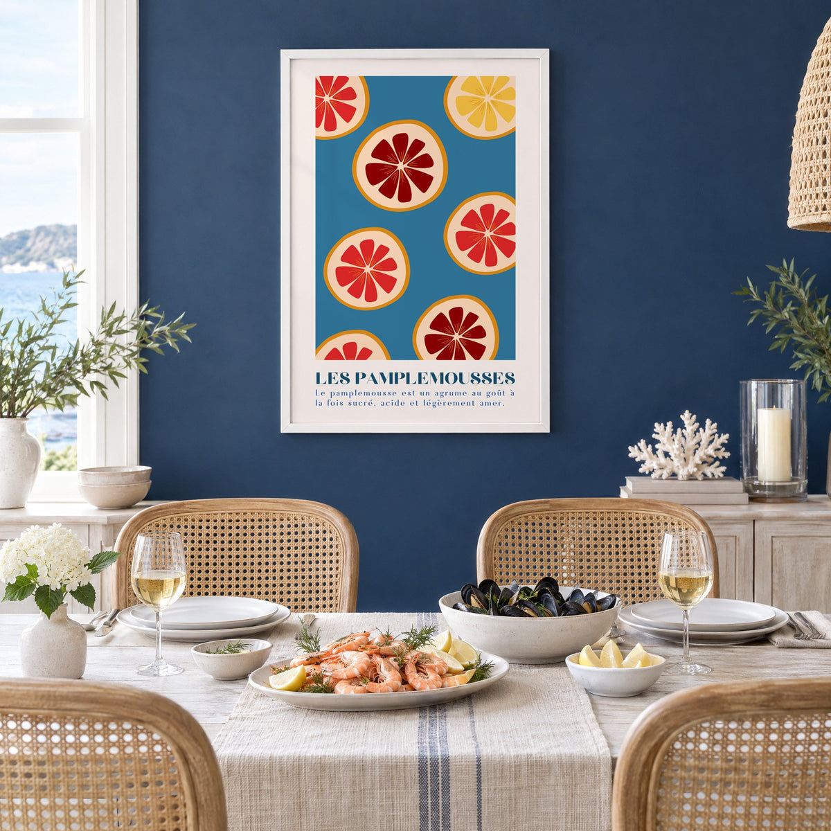 LES PAMPLEMOUSSES grapefruit slices petrol blue print in a white frame on a navy wall above a dining table set with shrimp and mussels