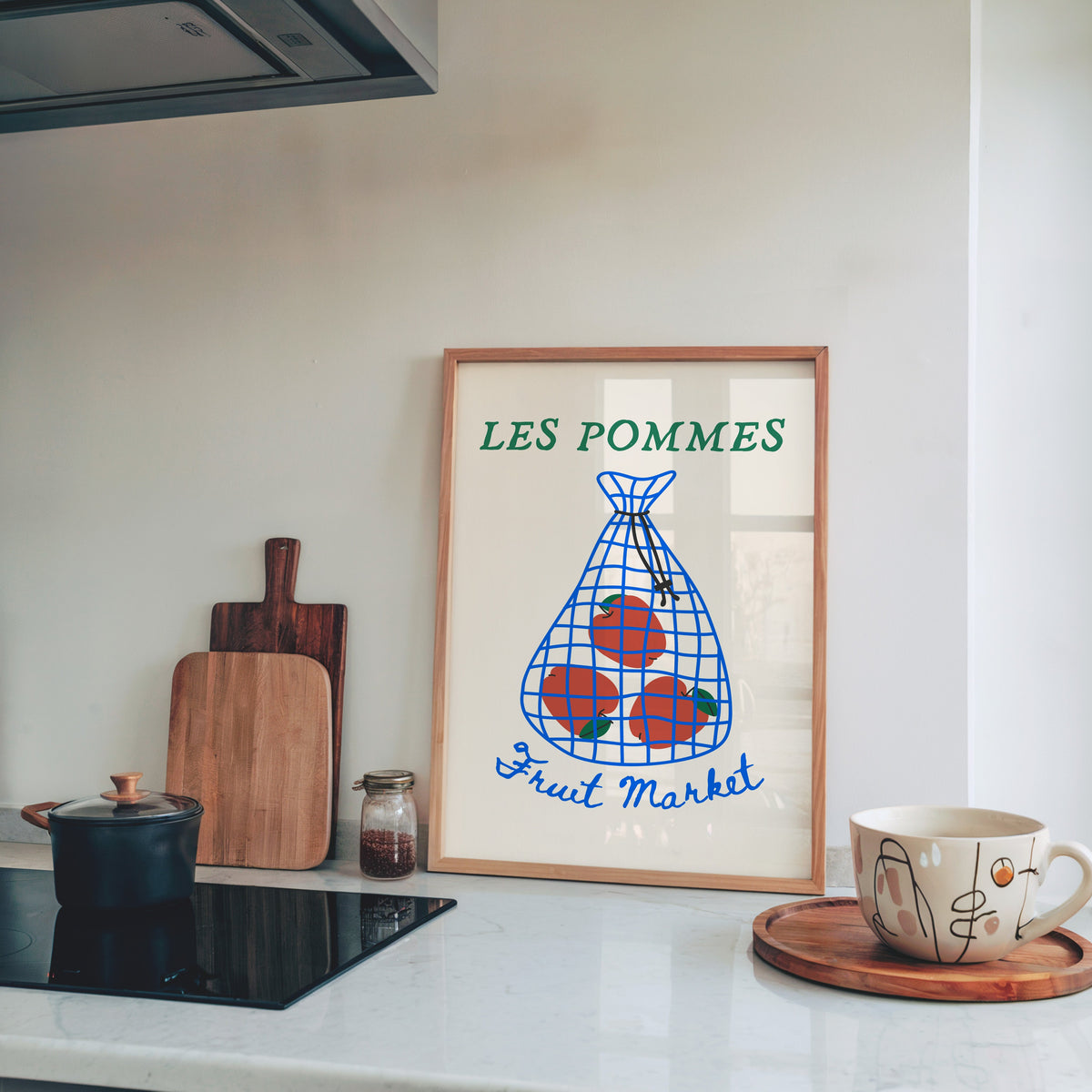 Les Pommes apples in a net bag print in a pine frame leaning on a marble kitchen counter beside chopping boards
