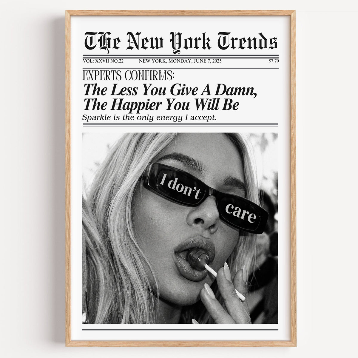 I don't care glasses and lollipop mock newspaper print in a light oak frame on a plain white wall
