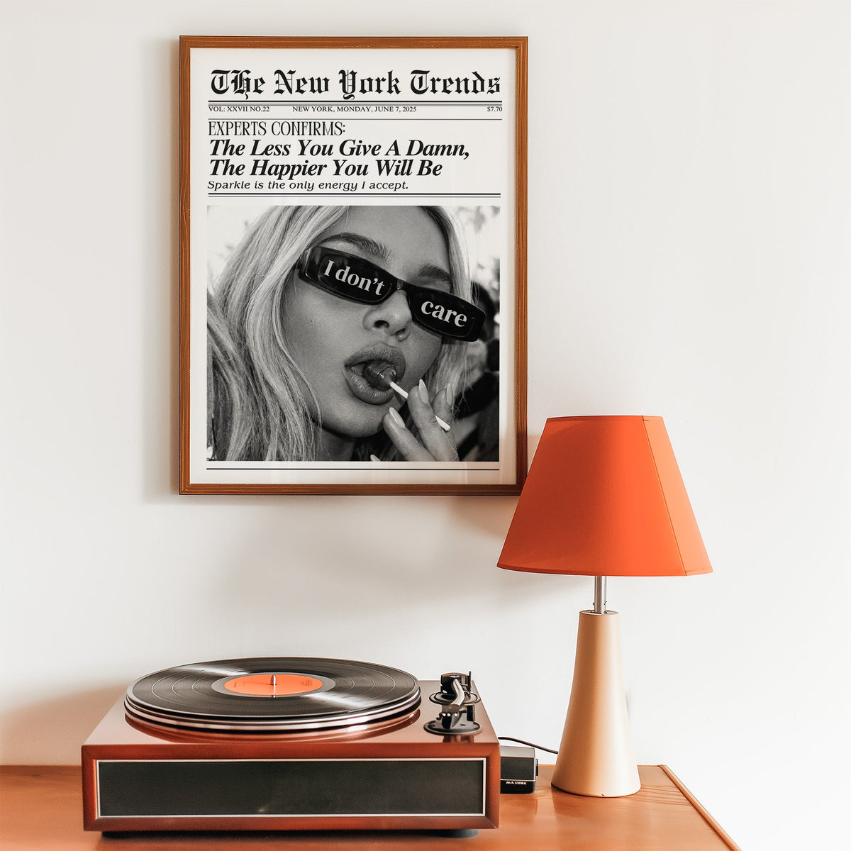 I don't care glasses and lollipop mock newspaper print in a walnut frame above a record player and orange lamp