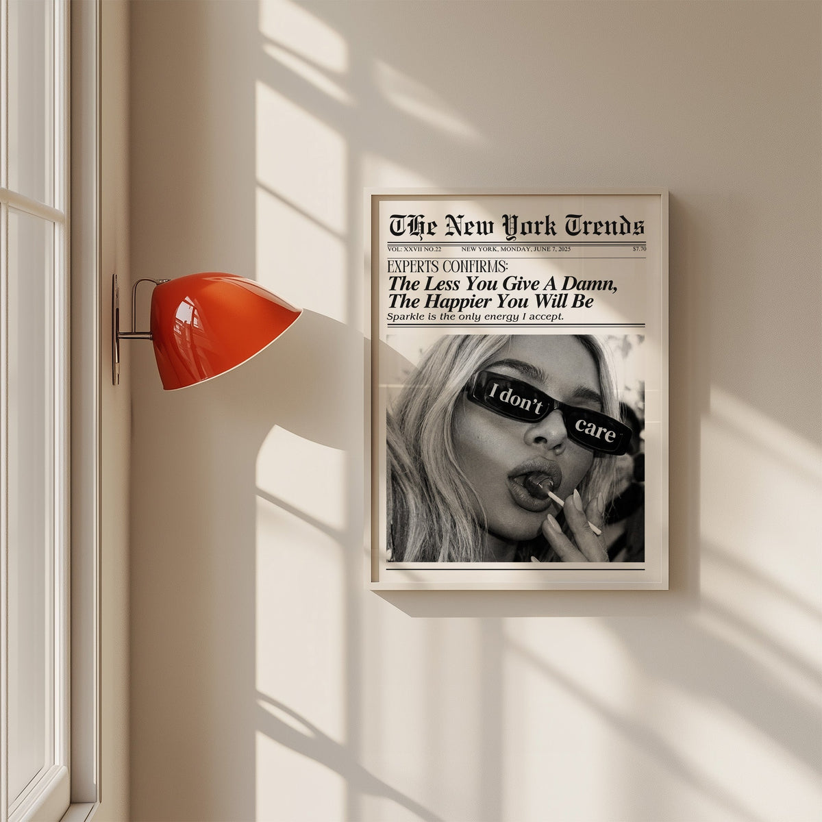 I don't care glasses and lollipop mock newspaper print in a white frame on a sunlit wall beside a red sconce