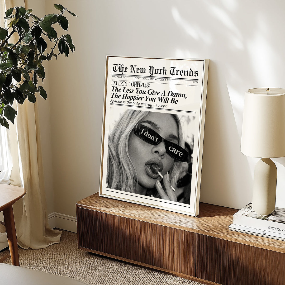 I don't care glasses and lollipop mock newspaper print in a white frame on a walnut sideboard beside a ceramic lamp
