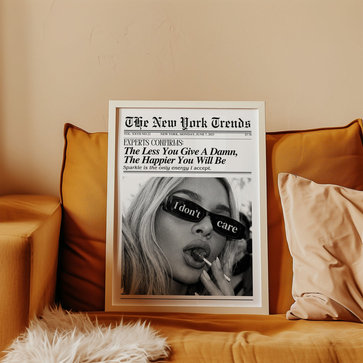 I don't care glasses and lollipop mock newspaper print in a white frame leaning on a mustard velvet sofa