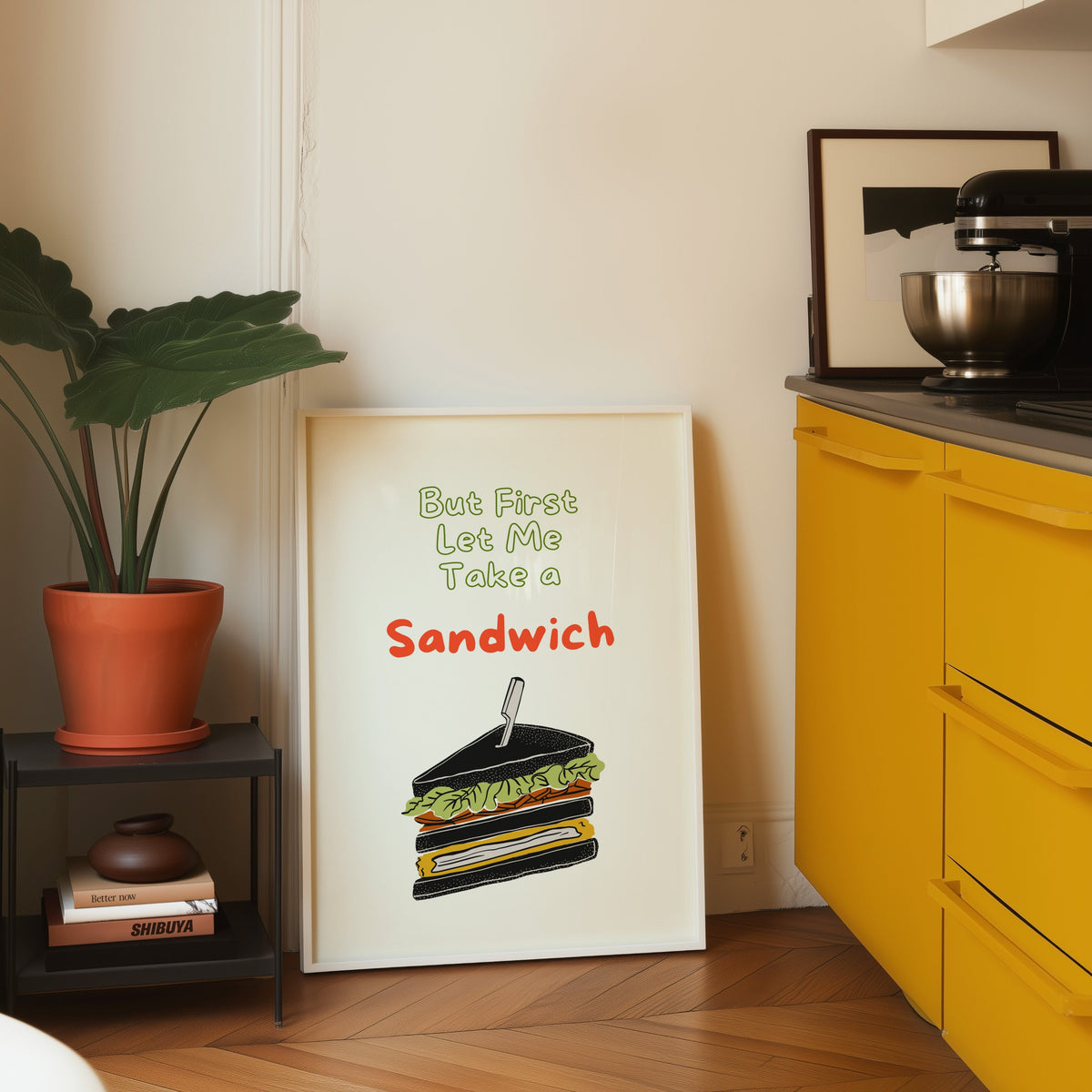 Club sandwich print in a white frame leaning on parquet beside a bright yellow kitchen