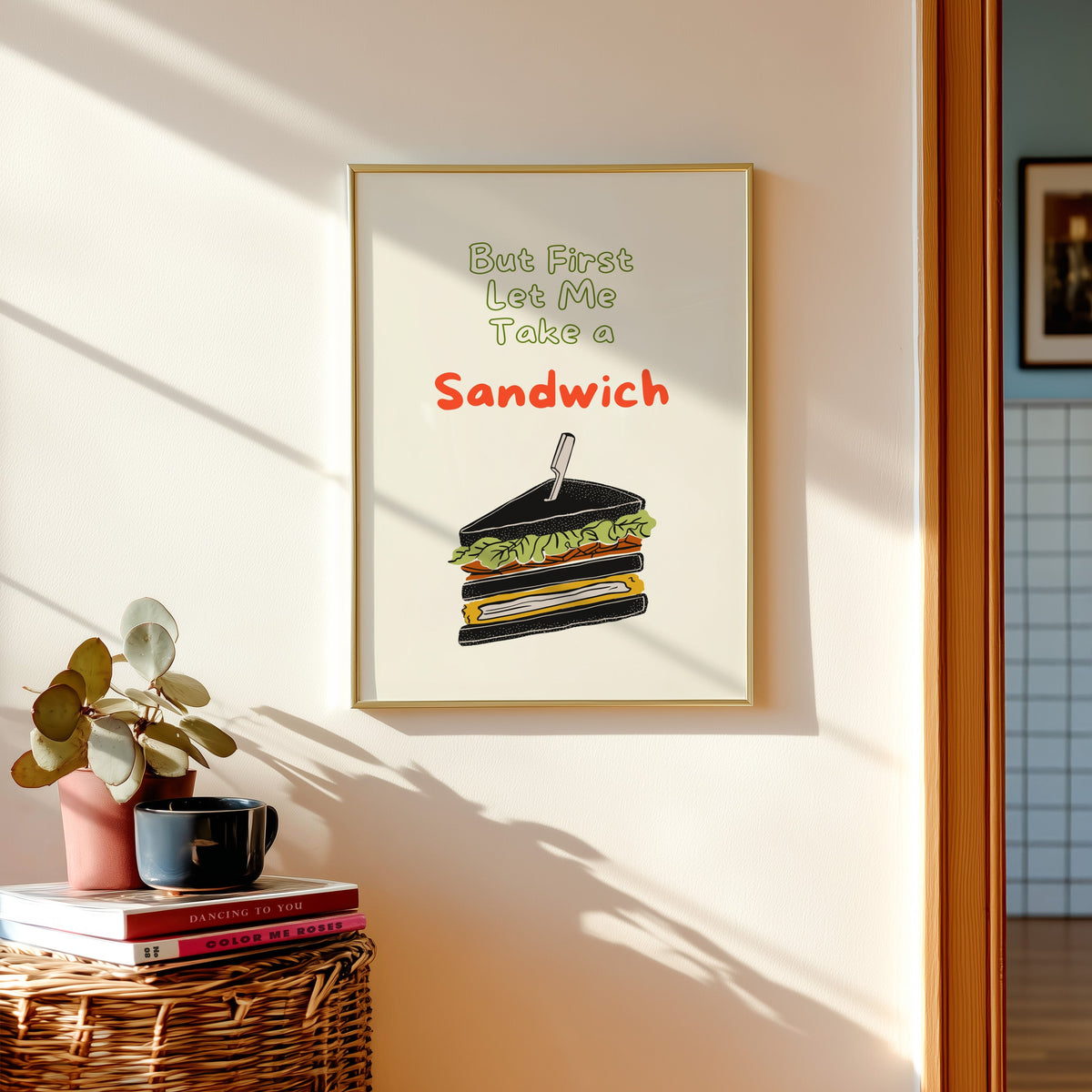 Club sandwich print shown in a gold frame above a basket of books and a pilea plant