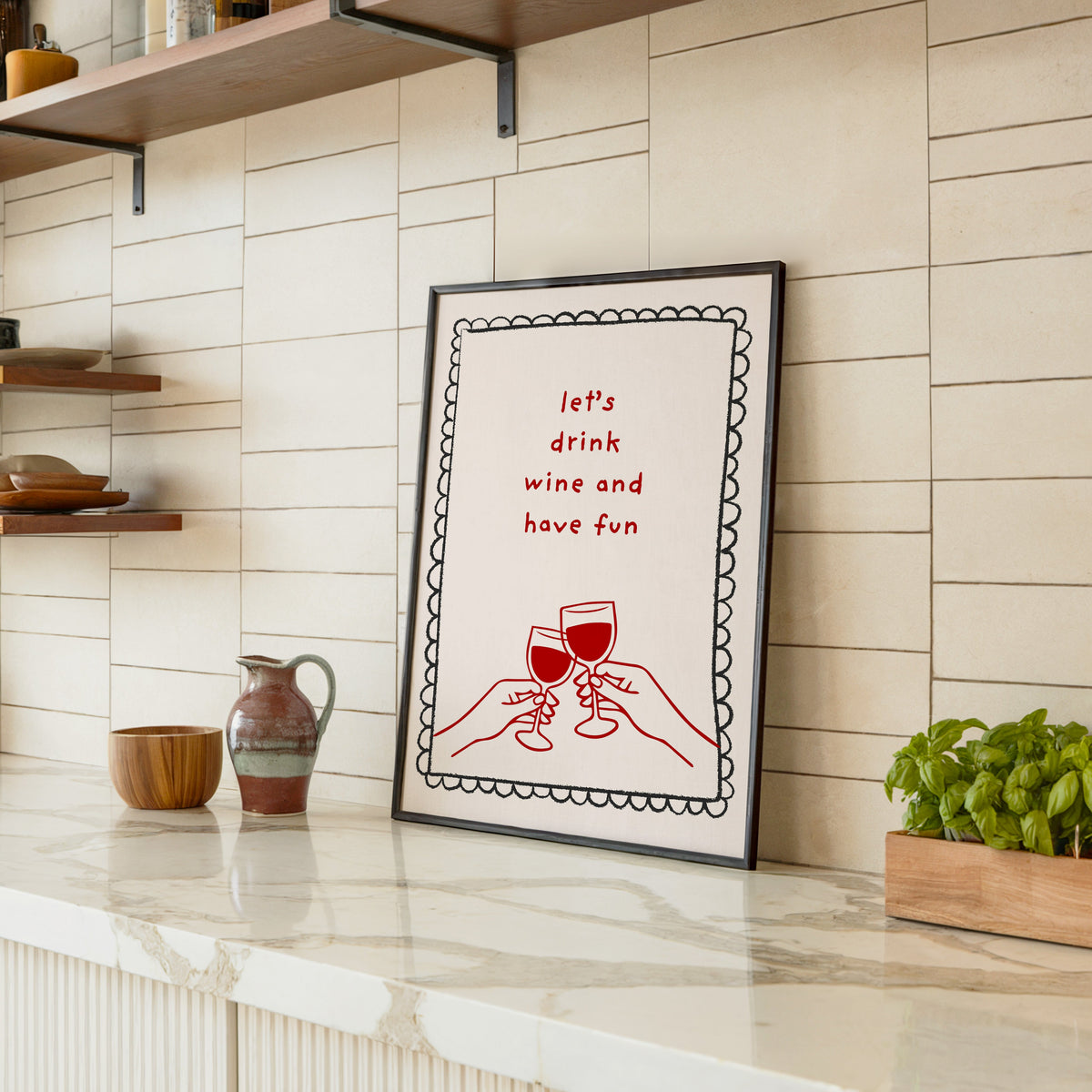 Lets Drink Wine and Have Fun print in a black frame leaning on a marble counter in a tiled kitchen