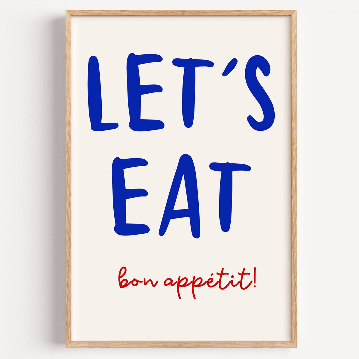 Let's Eat cobalt blue type print in a light oak frame on a plain white wall