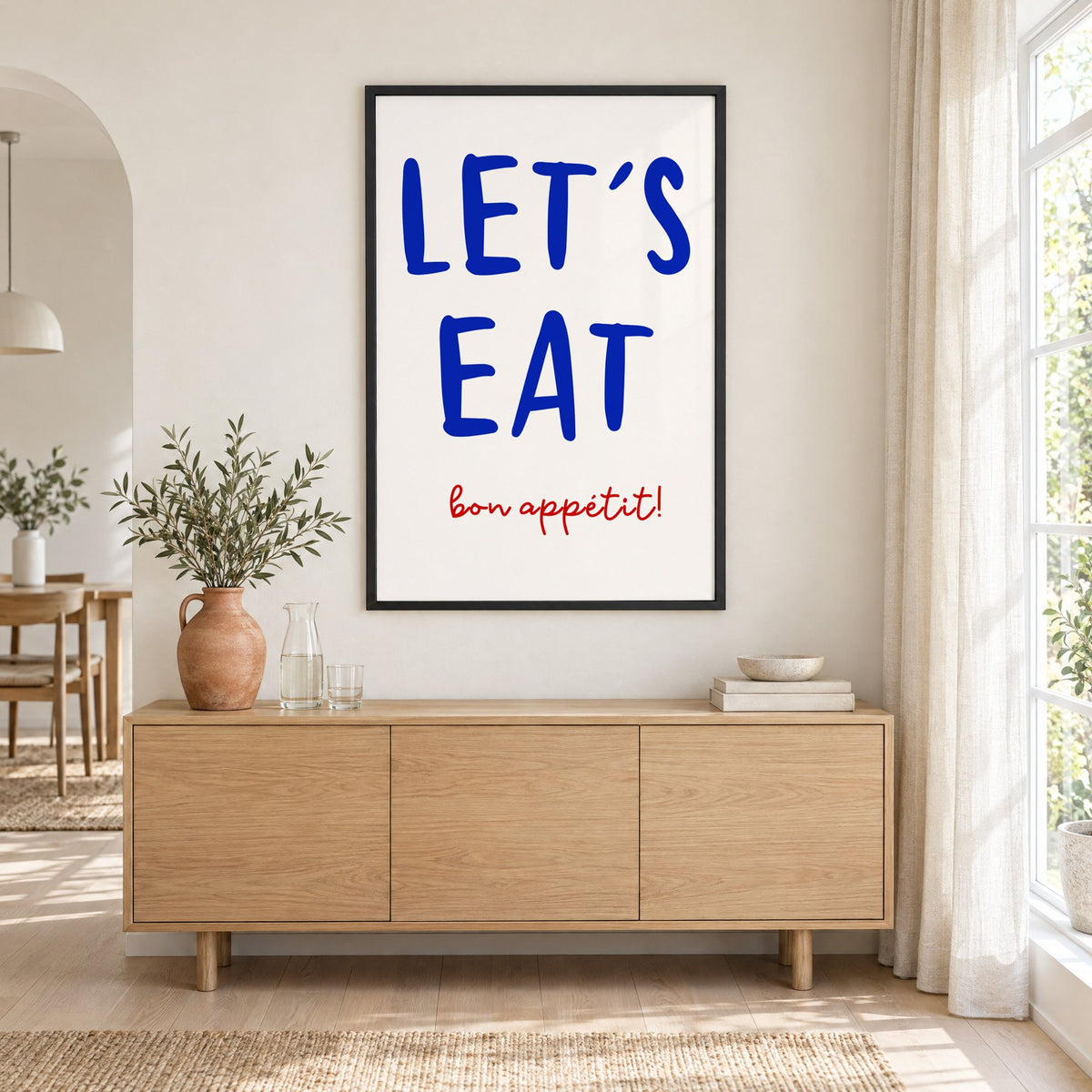Let's Eat cobalt blue type print in a black frame above an oak sideboard with a terracotta vase of olive branches