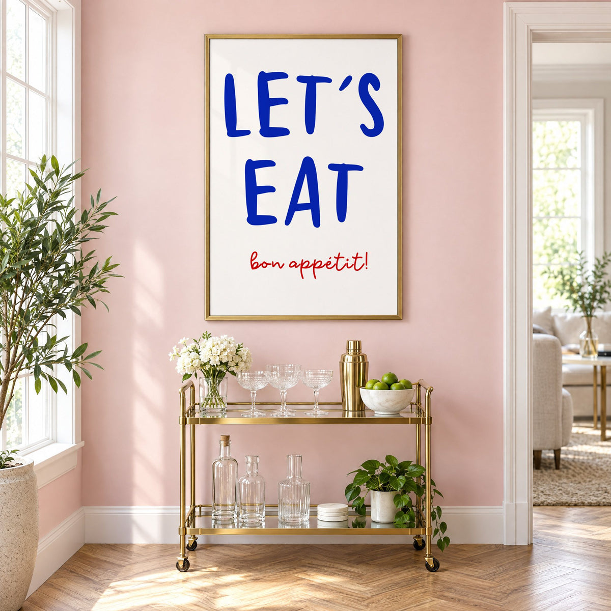 Let's Eat cobalt blue type print in a brass frame above a gold bar cart on a blush pink wall