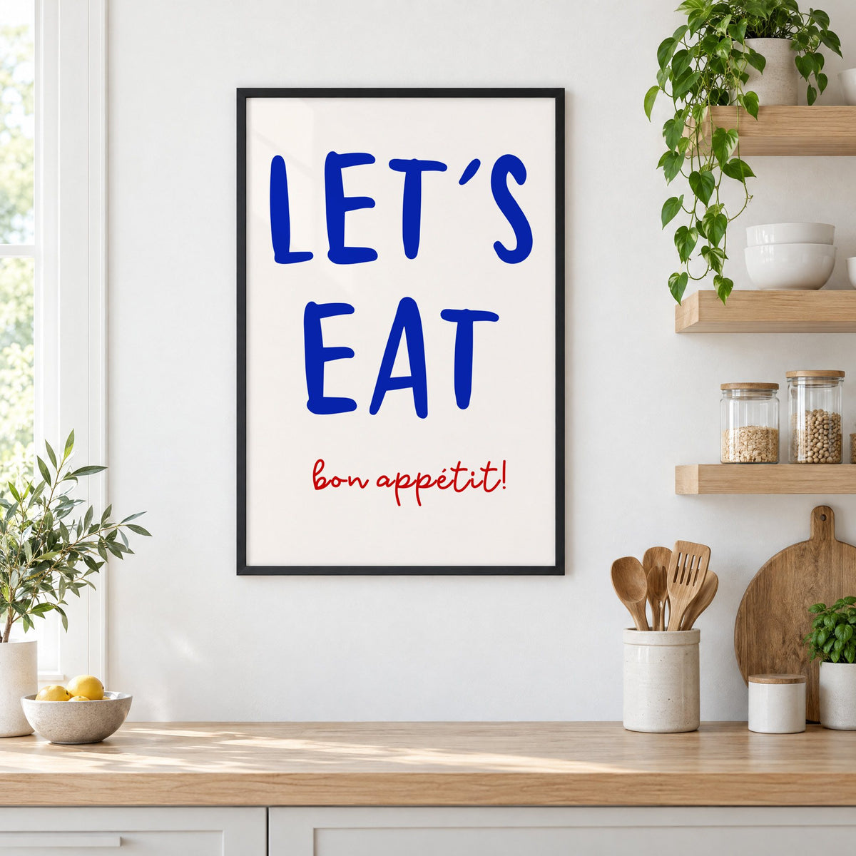 Let's Eat cobalt blue type print in a black frame in a white kitchen beside open wood shelves and glass jars