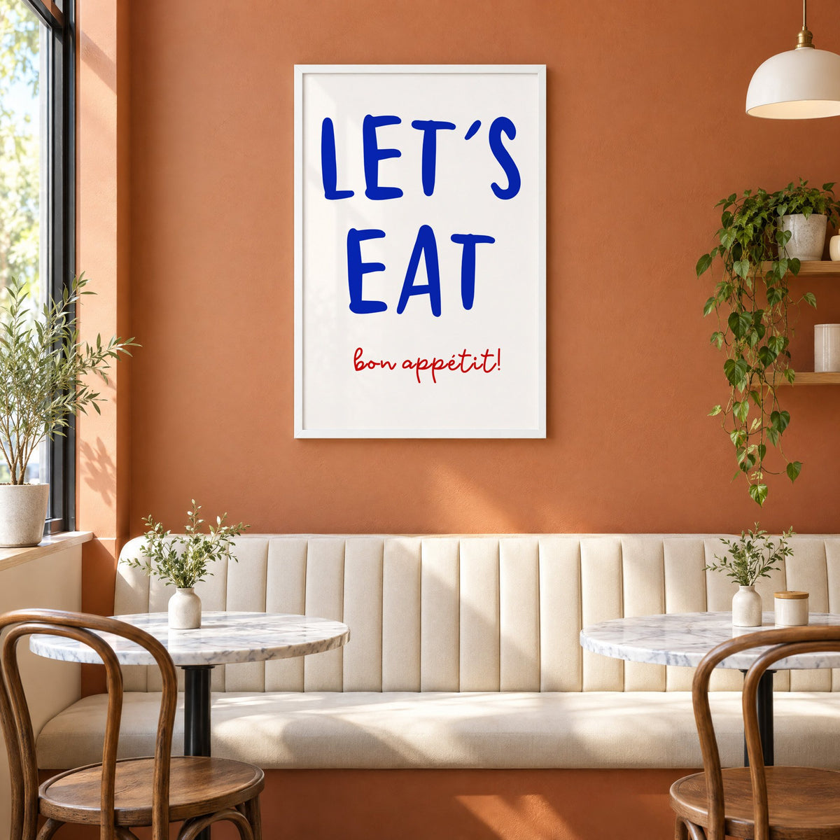 Let's Eat cobalt blue type print in a white frame above a cream banquette on a terracotta cafe wall