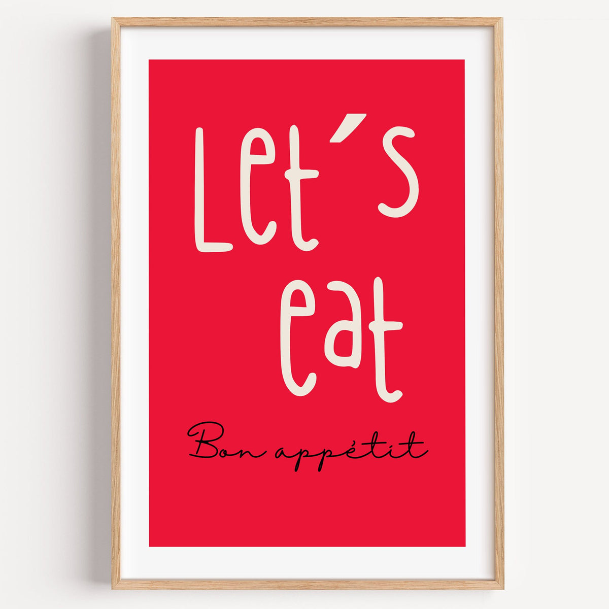 Let's eat red block print in a light oak frame on a plain white wall