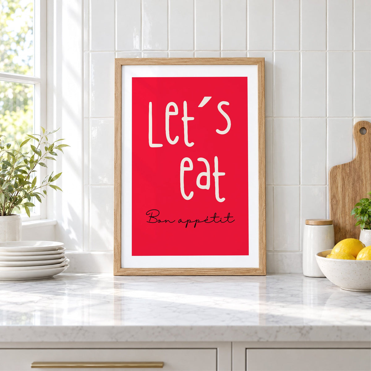 Let's eat red block print in an oak frame leaning on a marble counter by white tiles and lemons