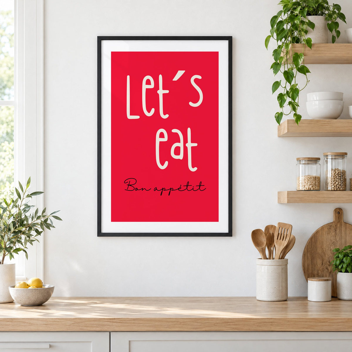 Let's eat red block print in a black frame in a white kitchen beside open wood shelves and glass jars