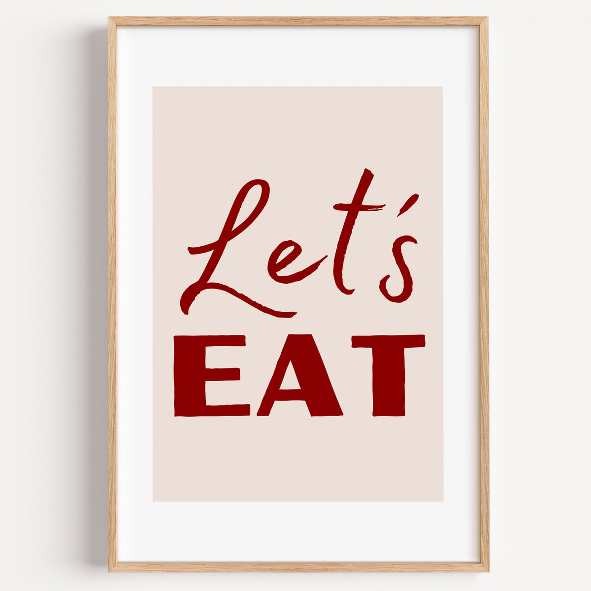 Let's EAT burgundy script print in a light oak frame on a plain white wall