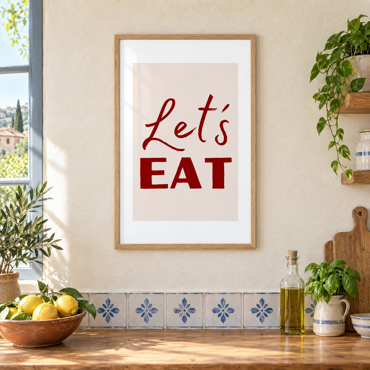 Let's EAT burgundy script print in an oak frame on a cream plaster wall above a worktop with a bowl of lemons and blue-and-white tiles