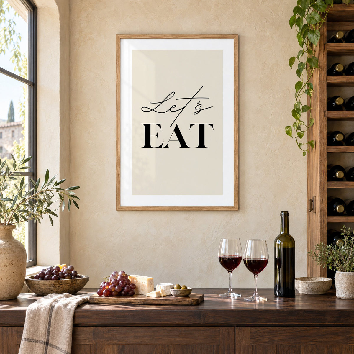 Let's EAT serif and script print in an oak frame on a limewashed wall above a wine counter with red wine, cheese and grapes