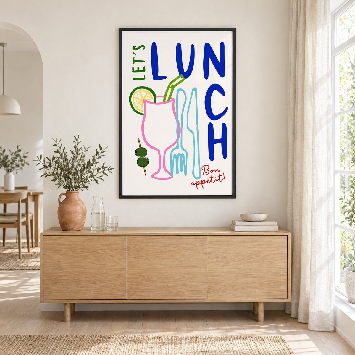 Let's Lunch cocktail and cutlery print in a black frame above an oak sideboard with a terracotta vase of olive branches