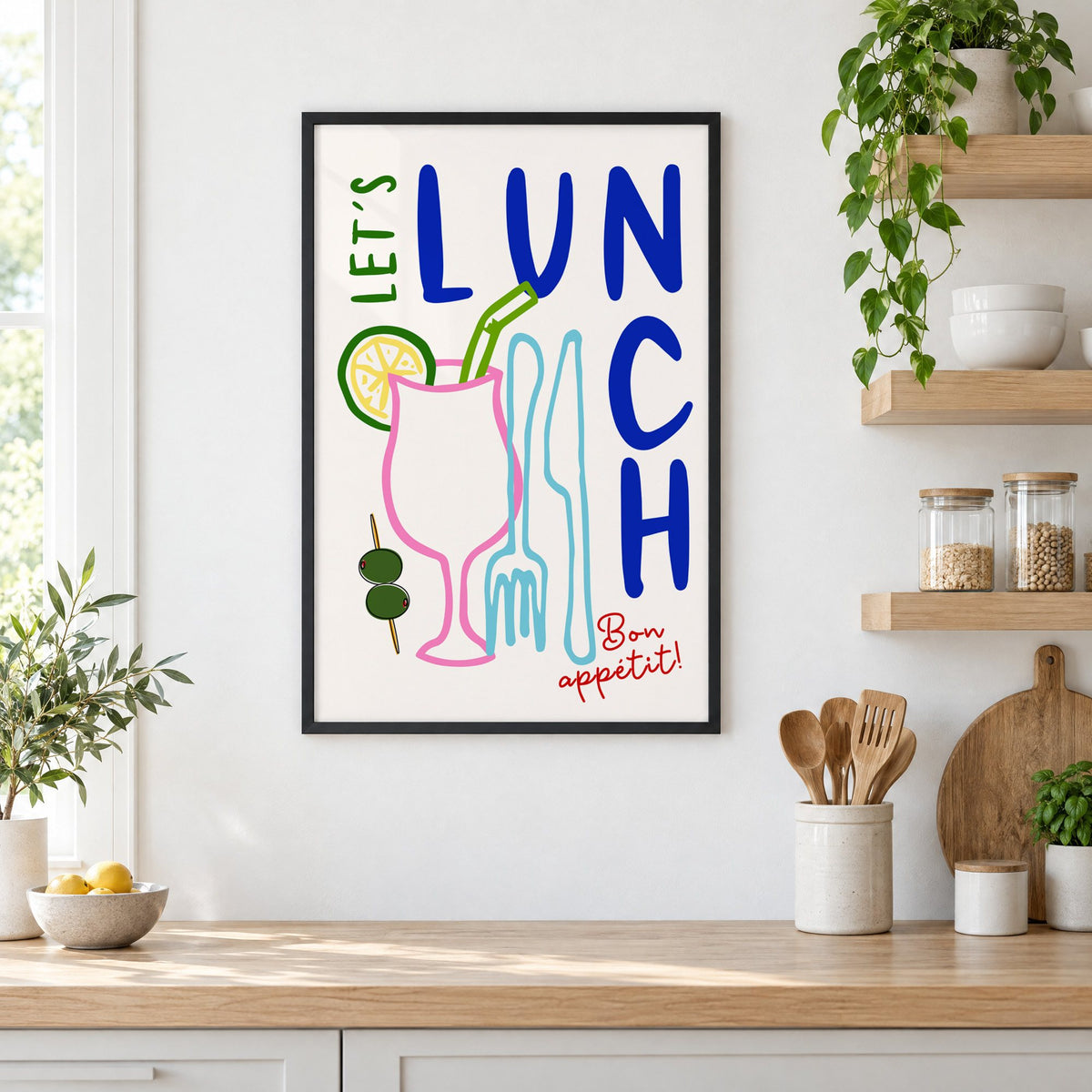 Let's Lunch cocktail and cutlery print in a black frame in a white kitchen beside open wood shelves and glass jars