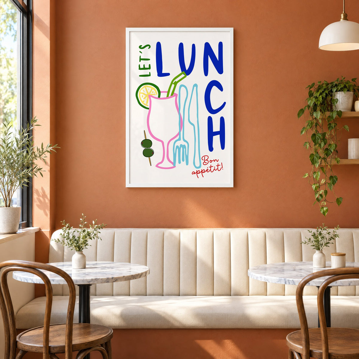 Let's Lunch cocktail and cutlery print in a white frame above a cream banquette on a terracotta cafe wall