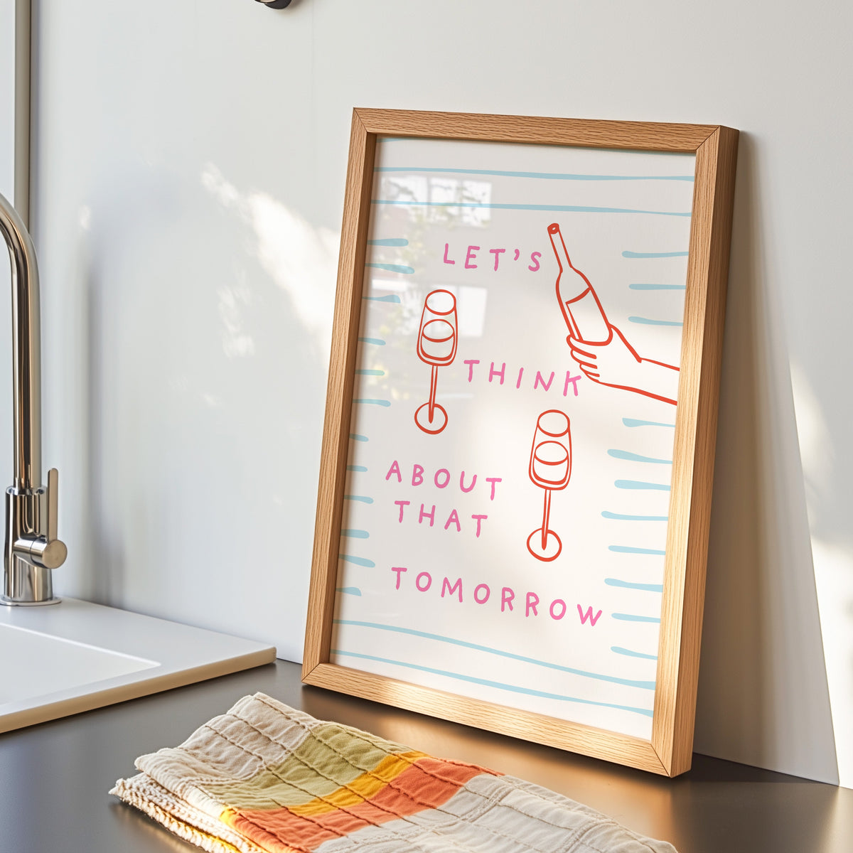 Wine pour line print in an oak frame by the kitchen sink beside a striped tea towel