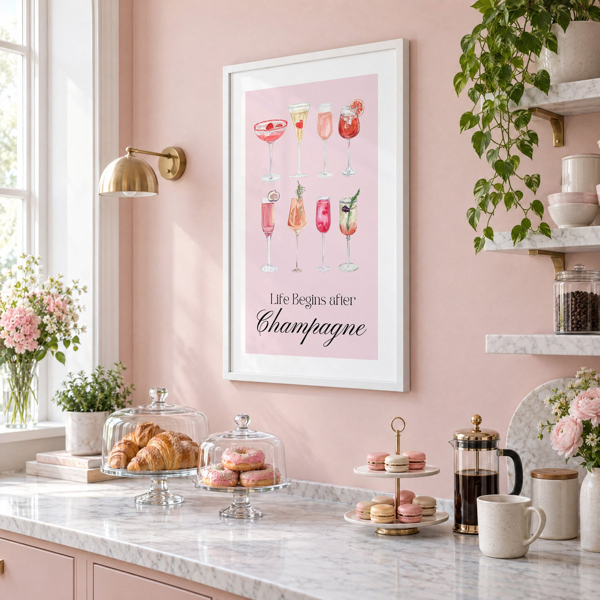 Life Begins after Champagne watercolor glasses print in a white frame on a blush pink wall above a patisserie counter with croissants and macarons, seen at an angle