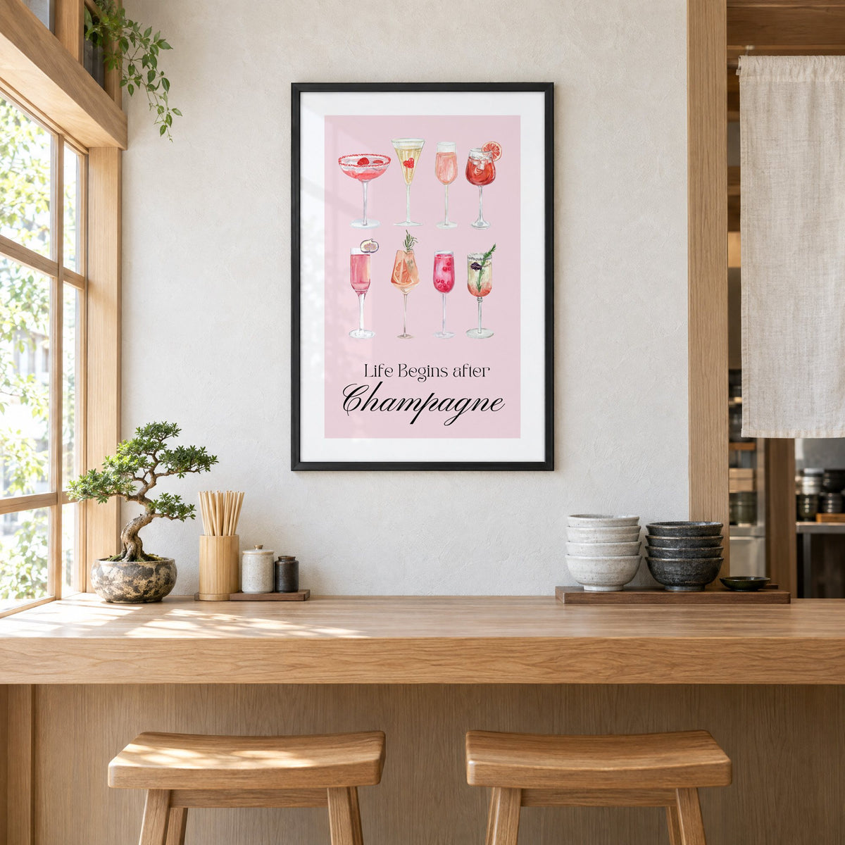 Life Begins after Champagne watercolor glasses print in a black frame above a light wood ramen counter with stools and stacked bowls