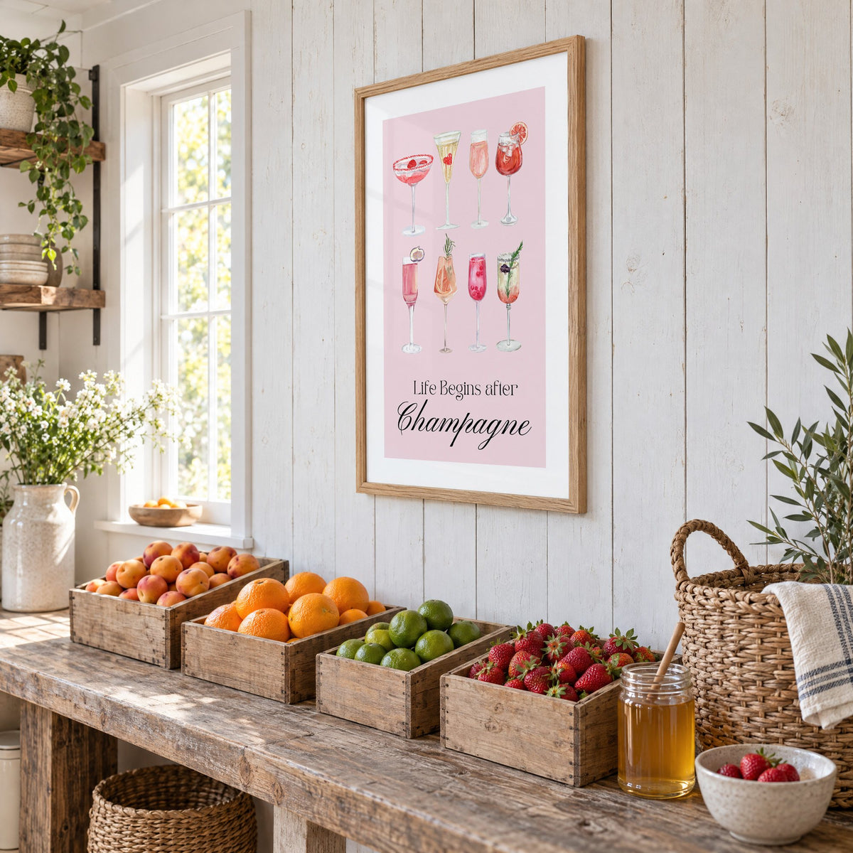 Life Begins after Champagne watercolor glasses print in an oak frame on white plank walls above wooden crates of fresh fruit, seen at an angle