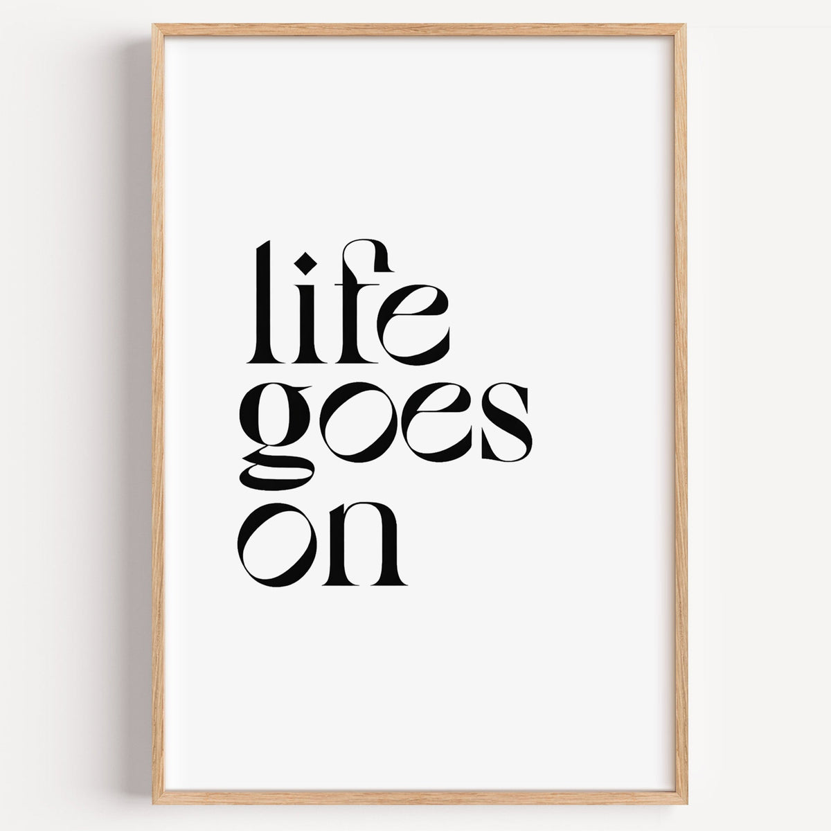 Life goes on serif quote print in a light oak frame on a plain white wall