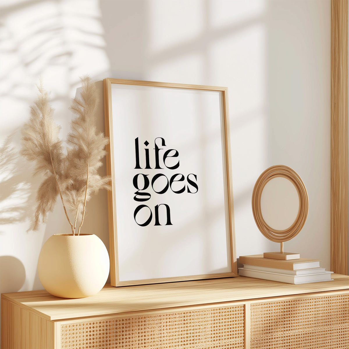 Life goes on serif quote print in an oak frame on a rattan sideboard beside pampas grass