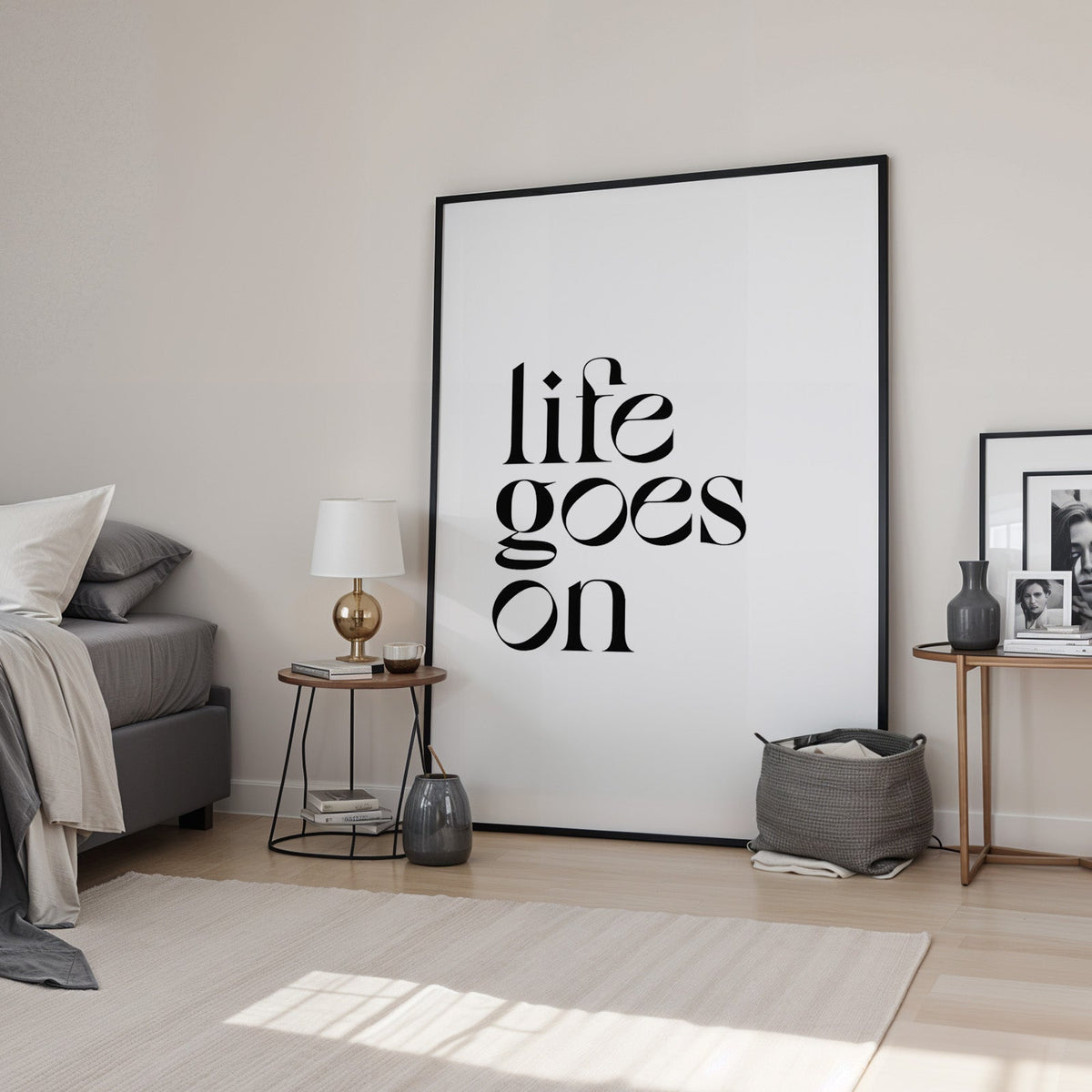 Life goes on serif quote print in a black frame leaning in a bedroom beside a gold lamp