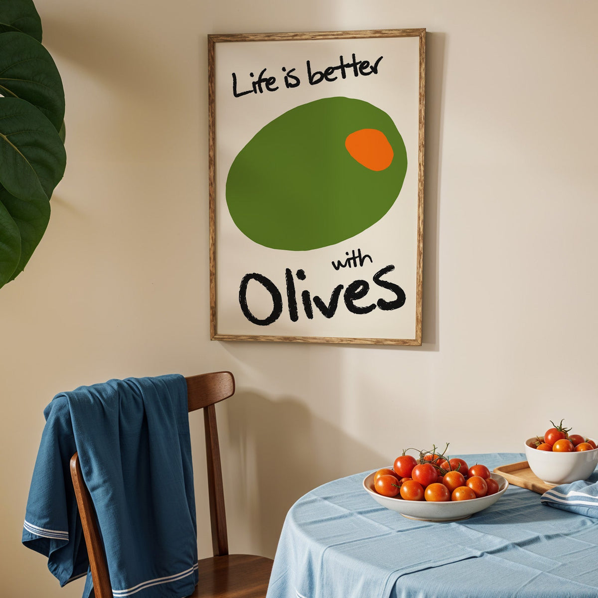 Life is better with olives print in an oak frame above a blue linen table with tomatoes