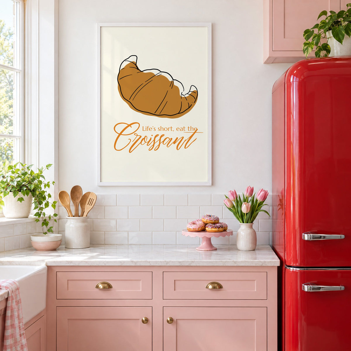 Life's short, eat the Croissant print in a white frame above pink cabinets beside a red retro fridge