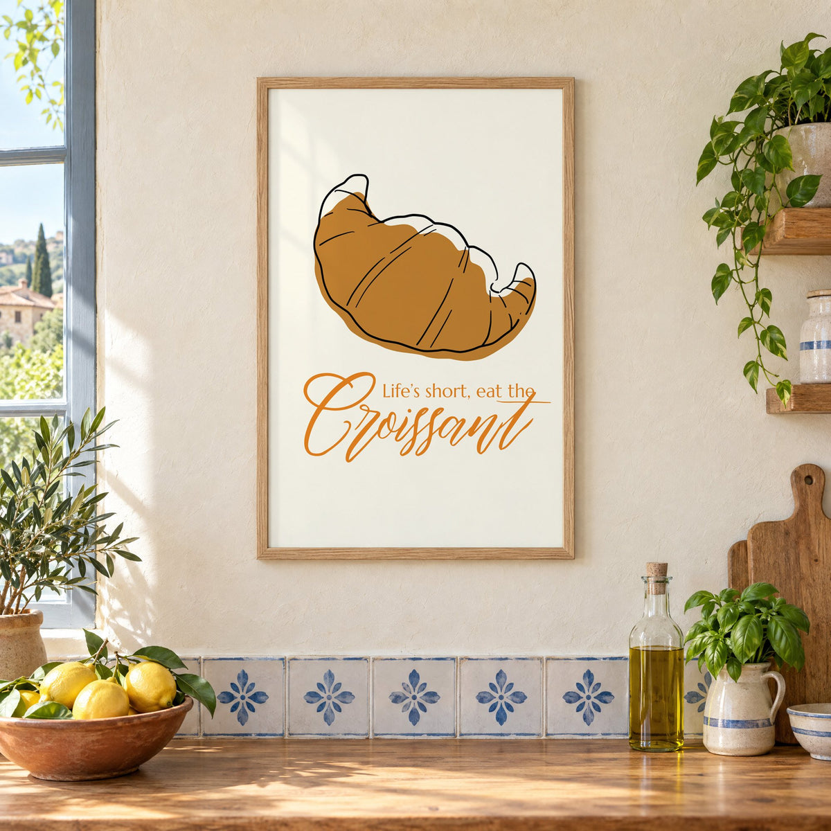 Life's short, eat the Croissant print in an oak frame on a cream plaster wall above a worktop with a bowl of lemons and blue-and-white tiles